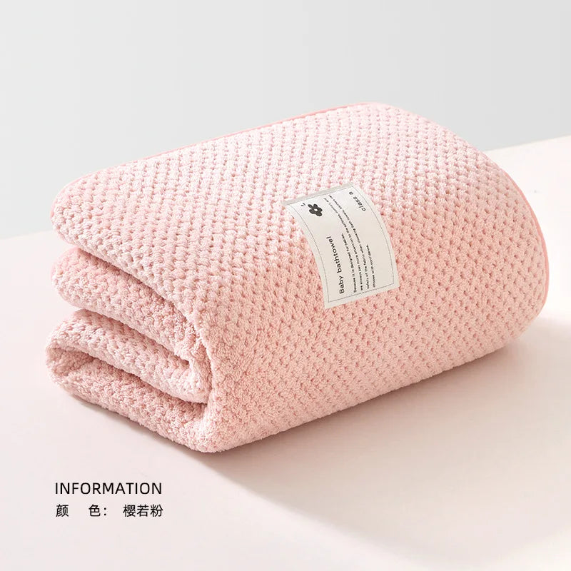 Une couverture tricotée rose douce soigneusement pliée sur une surface de couleur claire avec une étiquette BABY PREMA qui comprend les informations produit Lange Couverture Bébé 105X105cm, dégageant une sensation de chaleur et de confort pour un bébé prématuré.