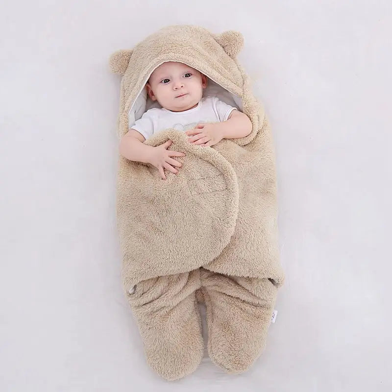 Un bébé douillet niché dans une gigoteuse BABY PREMA sur le thème de l'ours en peluche, avec seulement la tête et les mains qui ressortent, l'air douillet et adorable, entouré de tout le nécessaire pour bébé.