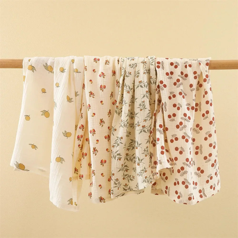 Five BABY PREMA Couverture Emmaillotage | en coton pour Bébé suspendu à une tige en bois sur fond jaune pâle, indispensable à l'hygiène de bébé.