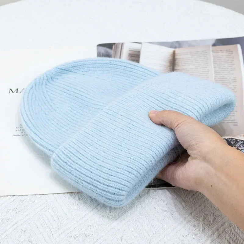 Une main appuyant doucement sur un bonnet Bonnet Angora Pour Maman bleu bébé doux de BABY PREMA, un accessoire indispensable pour les bébés, placé sur un magazine ouvert avec un texte mettant en valeur la texture et la qualité du fil.