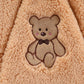 Motif ours en peluche brodé sur un tissu sherpa beige en peluche, représentant un ours souriant aux joues roses et un nœud papillon, offrant un confort maximal. Barboteuse à Capuche | Combinaison Epaisse Bébé de BABY-PREMA.