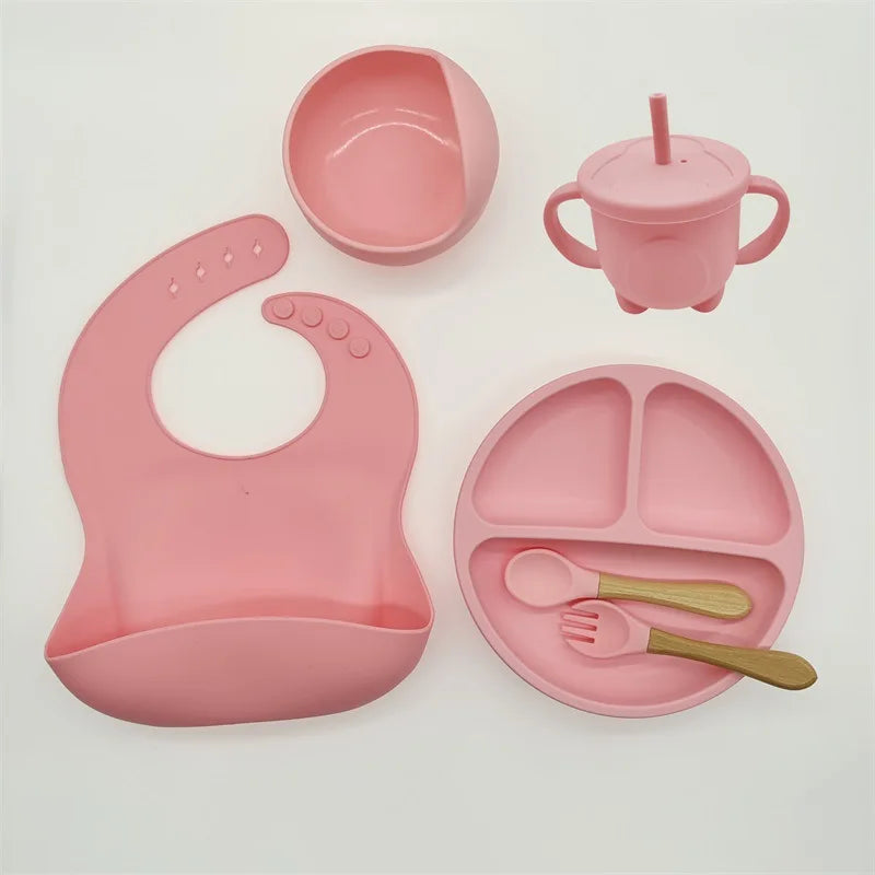 Un ensemble d'articles d'alimentation pour bébé roses en silicone de haute qualité, comprenant un bavoir, un bol, un gobelet, une assiette divisée, une fourchette et une cuillère. Cet Ensemble 6-8 Pièces de Vaisselle pour enfants de BABY PREMA est parfait pour votre tout-petit.