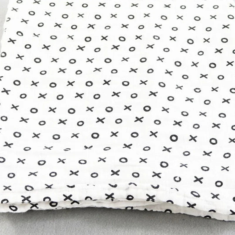 Une vue rapprochée d'un tissu avec un motif simple en noir et blanc, avec un motif répétitif de xs et d'os sur un fond pâle, parfait pour les accessoires bébé, la Couverture en Mousseline de Coton pour Bébé de BABY PREMA.