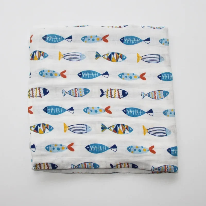 Une couverture en mousseline de coton pour bébé soigneusement pliée de BABY PREMA, présentant un motif coloré de poissons stylisés sur un fond blanc.