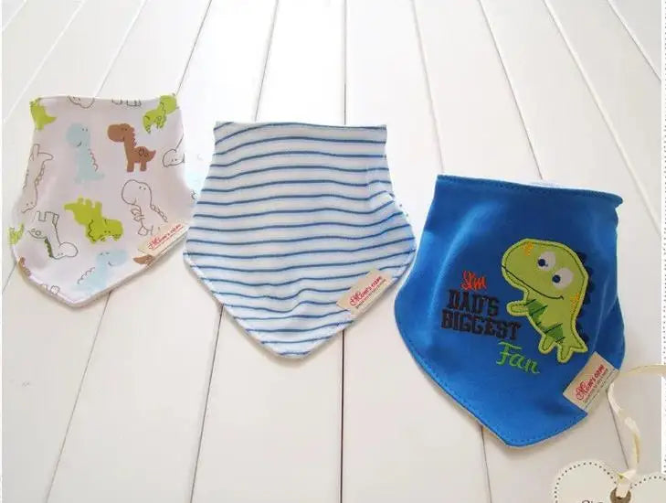 Trois bavoirs pour bébé sont disposés sur une surface en bois blanc. Le bavoir de gauche a un motif de dinosaure, celui du milieu est à rayures bleues et blanches, et celui de droite est bleu avec un dinosaure vert brodé et le texte « Je suis le plus grand fan de papa ». Ce charmant Lot de 3 Bavoirs 100% Coton de BABY-PREMA est composé de coton doux et résistant.